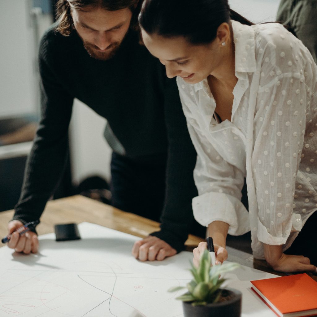 man-and-woman-leaning-on-table-staring-at-white-board-on-top-320550